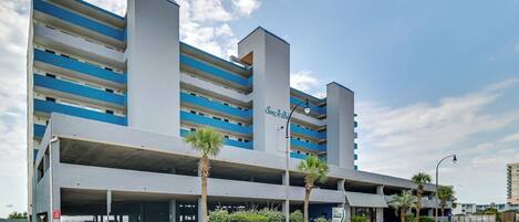 A multi-story parking garage with a blue and white color scheme, outdoor parking spaces, and a street view.