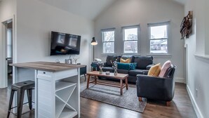A spacious living room with a modern sofa, a wooden coffee table, and a TV mounted on the wall. - King-bed Mural loft near 12 South with easy access to local attractions (Nashville)