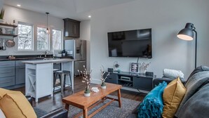 A modern kitchen with a central island, a dining area with a wooden table, and a living room with a sofa and a TV. - King-bed Mural loft near 12 South with easy access to local attractions (Nashville)