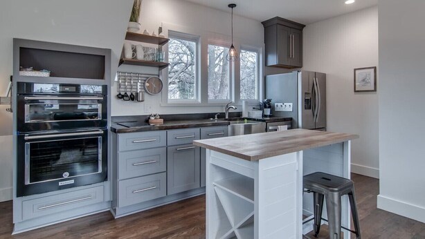 A modern kitchen with grey cabinetry, a built-in oven, a large island with stools, and a window providing natural light. - King-bed Mural loft near 12 South with easy access to local attractions (Nashville)
