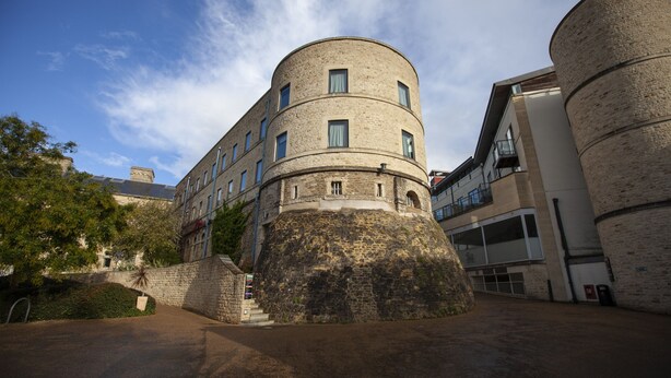 Un bâtiment historique doté d’une tour ronde, d’un mur en pierre et d’une extension moderne.