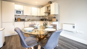 Une cuisine moderne avec des meubles blancs, une table à manger en verre et quatre chaises grises.