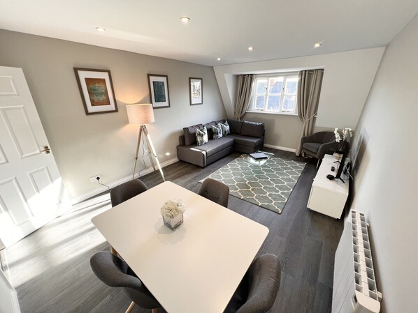 A modern living room with a dining area, grey sofas, a standing lamp, and a large window with curtains. - Beautiful central apartment with parking (Oxford)