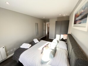 Una habitación de hotel moderna con una cama grande, una mesita de noche, un armario y vistas al pasillo.