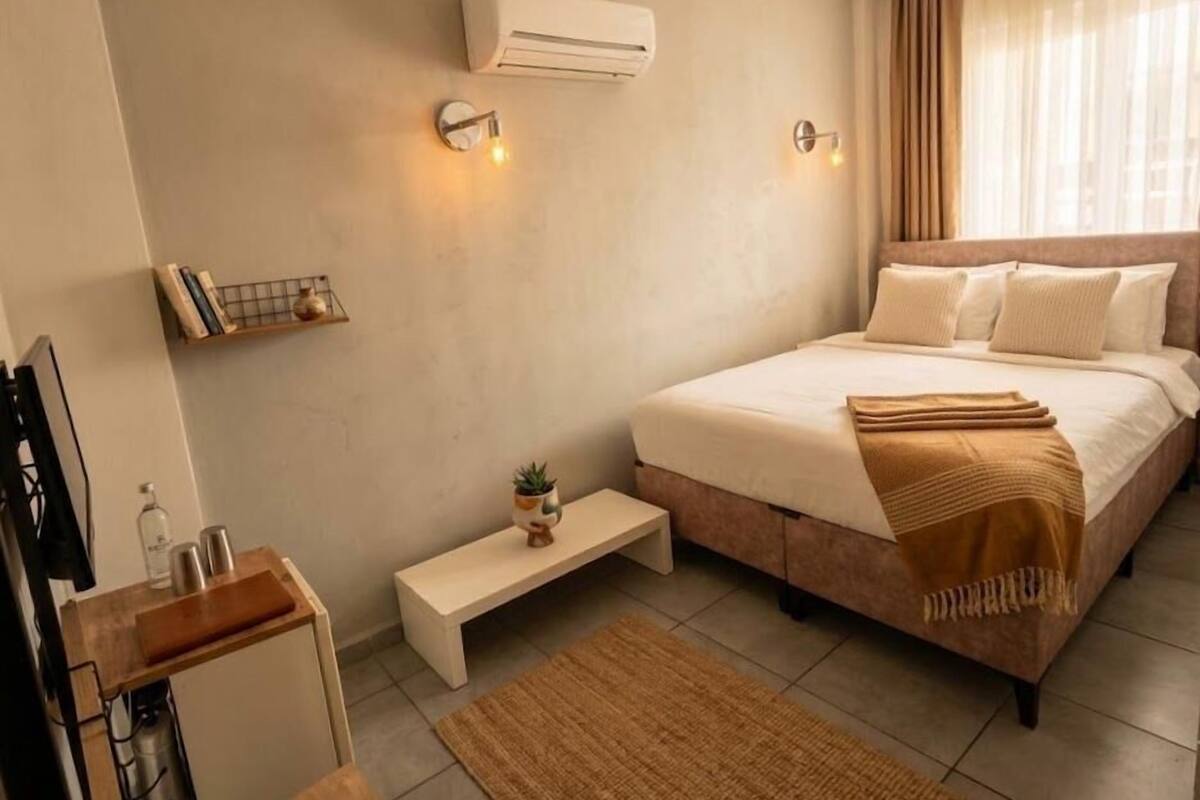 Un dormitorio con cama, mesitas de noche, un equipo de aire acondicionado y una ventana con cortinas.