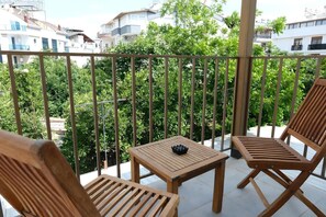 A balcony with wooden furniture, a small table, and a view of surrounding buildings and greenery. - Babil Hotel (Konyaalti)