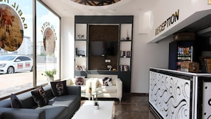 Uma área de recepção moderna com um sofá, uma mesa de centro e uma televisão presa na parede.