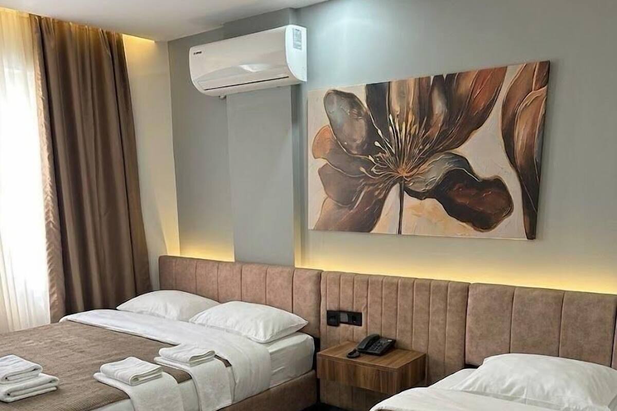 Habitación de hotel con dos camas, aire acondicionado de pared, un cuadro y una mesita de noche con teléfono.