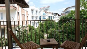Varanda com duas cadeiras de madeira e uma mesa, com vista para uma área residencial com edifícios e árvores.