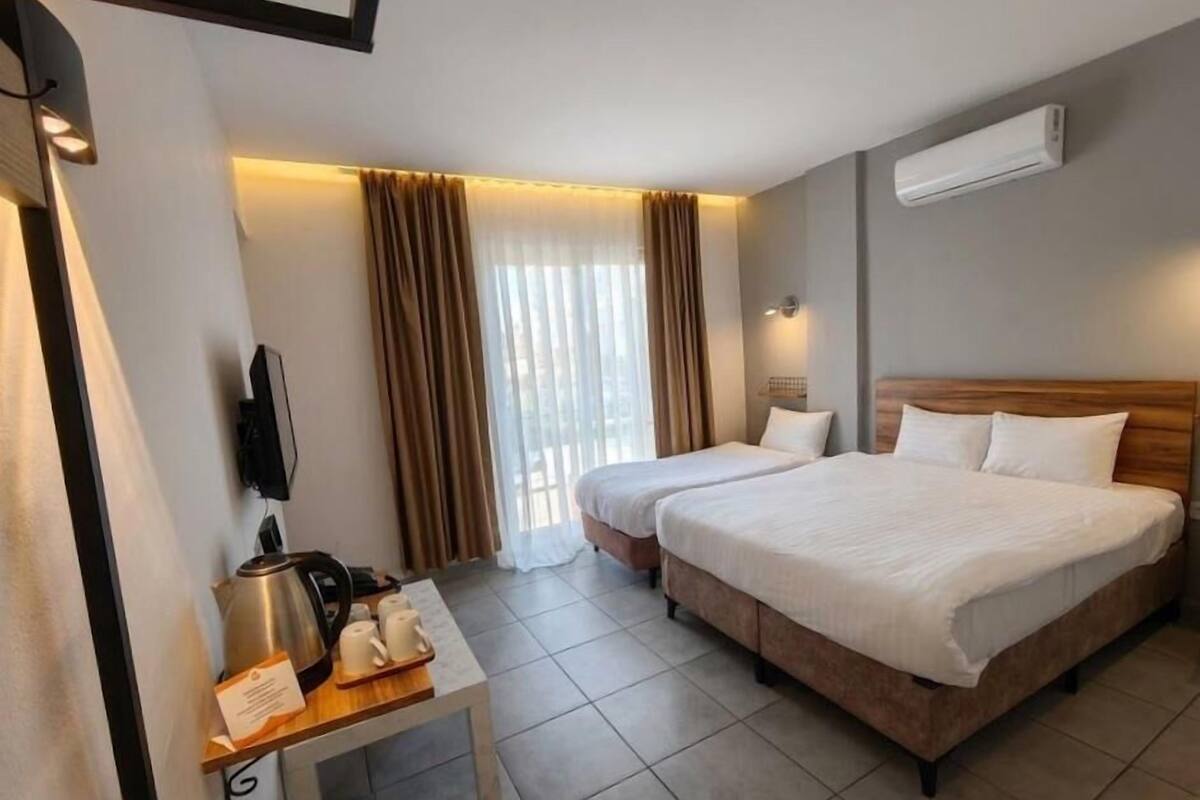 Una habitación de hotel con dos camas, un escritorio con una tetera y tazas, un televisor y aire acondicionado.
