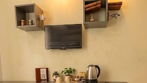 Uma cozinha moderna com televisão de tela plana, duas cadeiras, cafeteira e prateleiras com livros e potes.