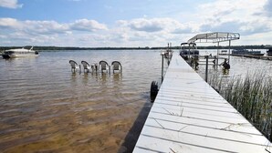 Un muelle de madera se extiende sobre un lago tranquilo de aguas cristalinas, rodeado de vegetación y una orilla distante.