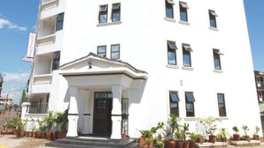 Un edificio blanco de varios pisos con una entrada central, balcones y plantas en macetas.
