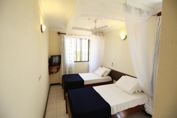 Quarto de hotel com duas camas, televisão e janela com cortinas.