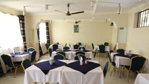 Un comedor con mesas y sillas redondas, ventiladores de techo y un ventanal con cortinas.