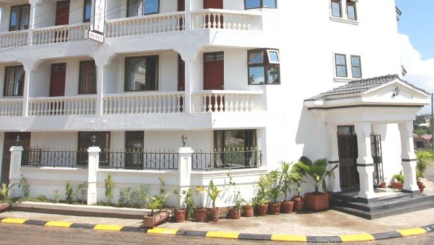 Un hotel de varios pisos con balcones, entrada protegida por un portón y plantas en macetas.
