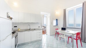 A modern kitchen with white cabinets, a tiled backsplash, and a dining area with a table and chairs. - Marina Grande - Gioia Apartments (Procida)
