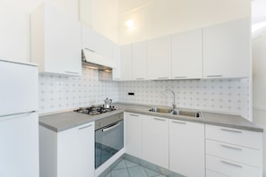 A modern kitchen with white cabinets, a gas stove, an oven, and a sink.