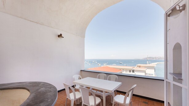 A balcony with a white table and chairs, a small heater, and a view of the sea with boats. - Marina Grande - Gioia Apartments (Procida)