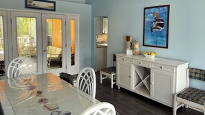 A dining area with a glass-top table, white chairs, and a white cabinet with drawers. - Silver Thatch -4BR home Close to the beach. Linens and Towels Provided. (Chincoteague)