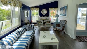 A living room with a blue sofa, a white coffee table, and a dining area with a table and chairs. - Silver Thatch -4BR home Close to the beach. Linens and Towels Provided. (Chincoteague)
