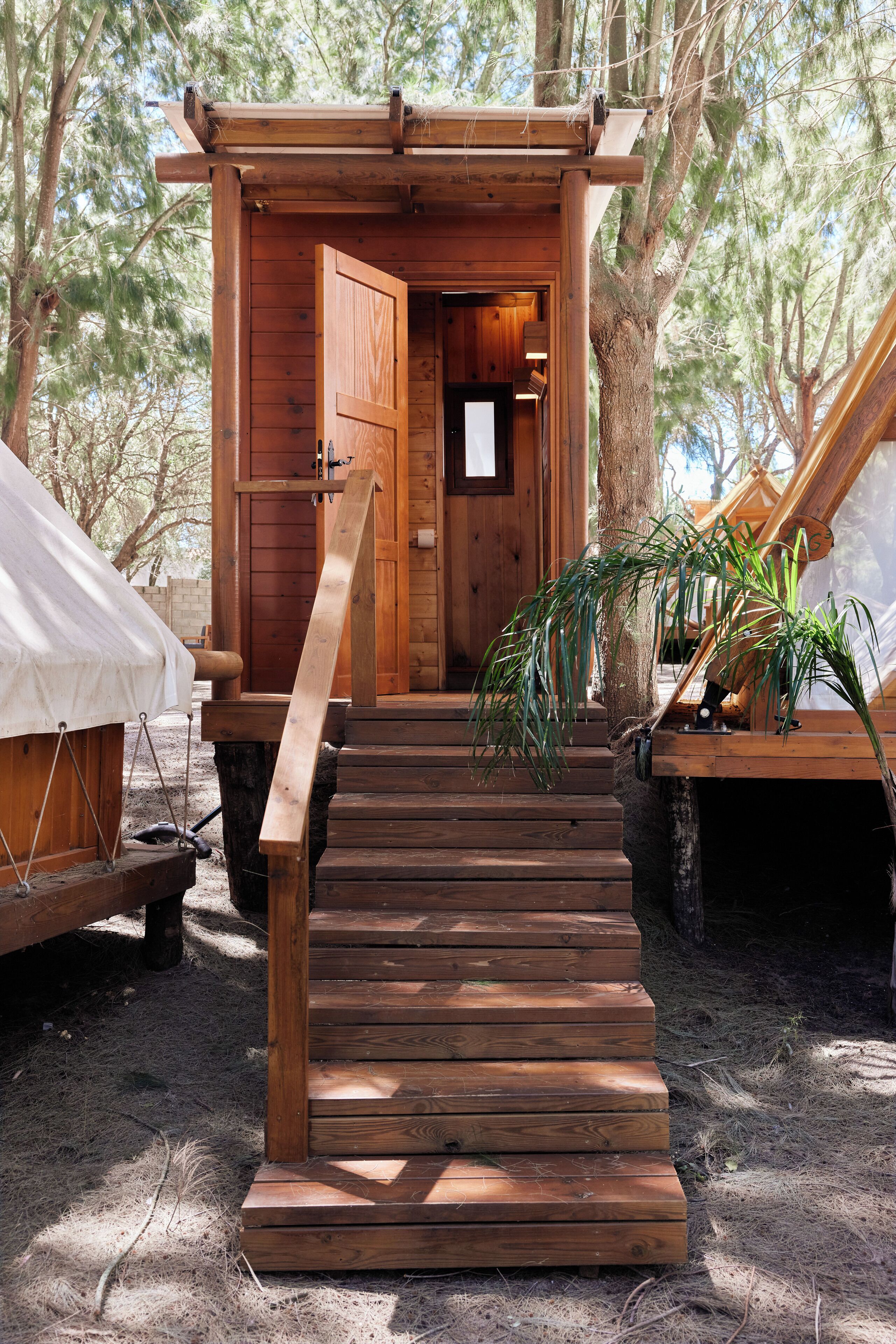 Una cabaña de madera con una escalera que lleva a una puerta, rodeada de árboles.