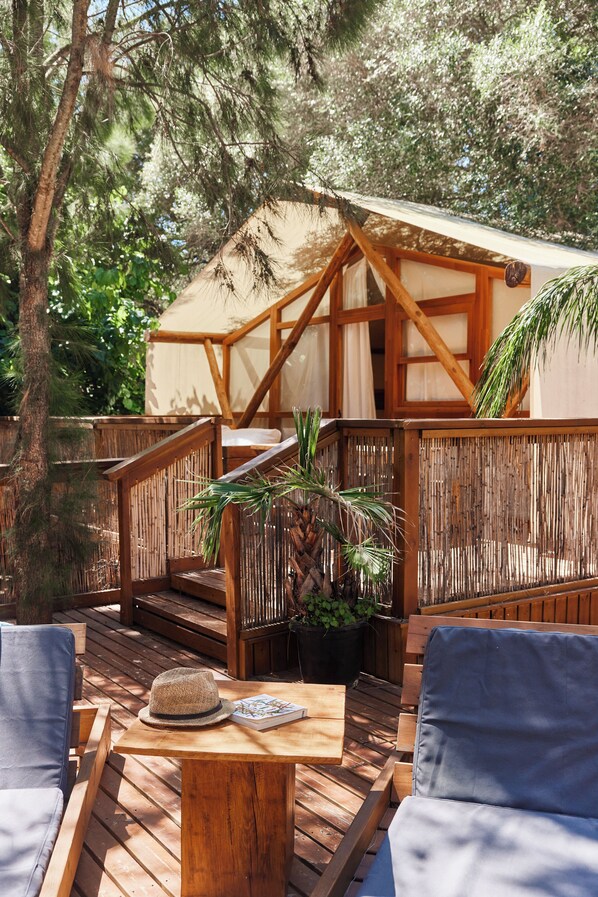 Una terraza de madera con mobiliario exterior, un espacio de estar cubierto y una estructura de madera con techo de paja.