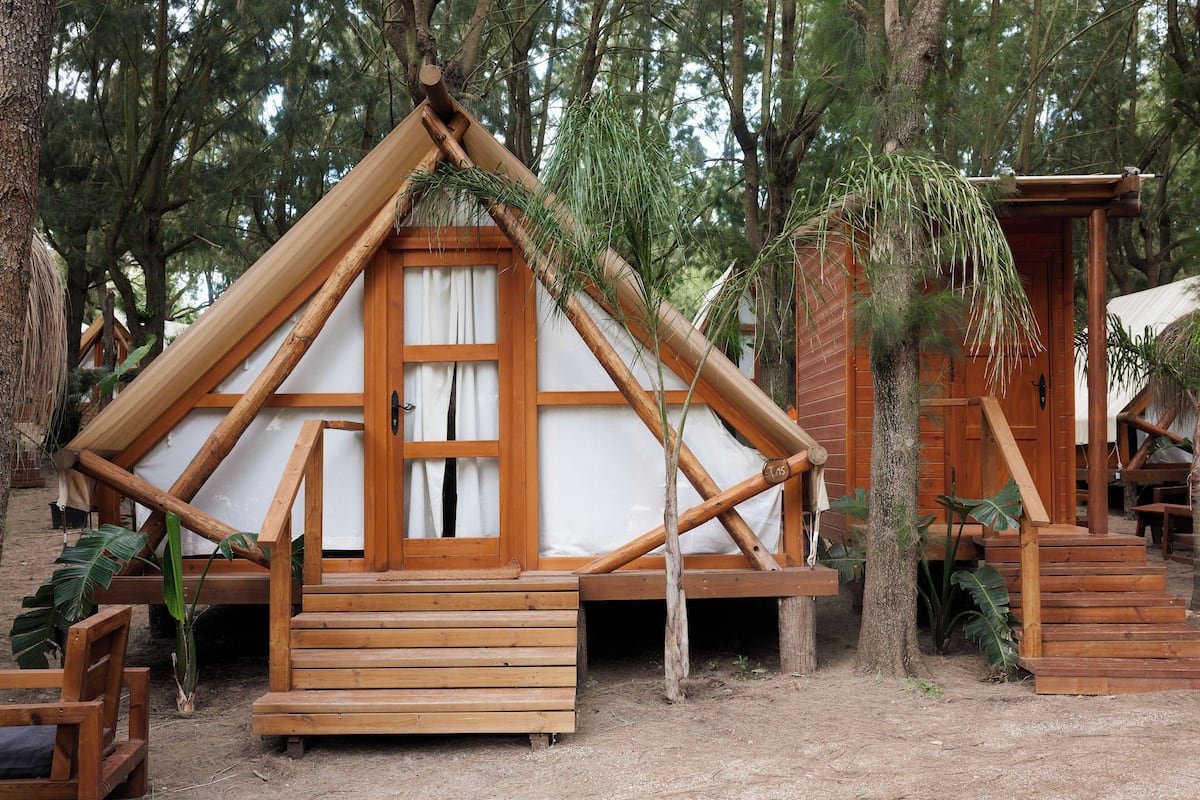 A wooden cabin with a triangular roof, a wooden porch, and a door with a window.