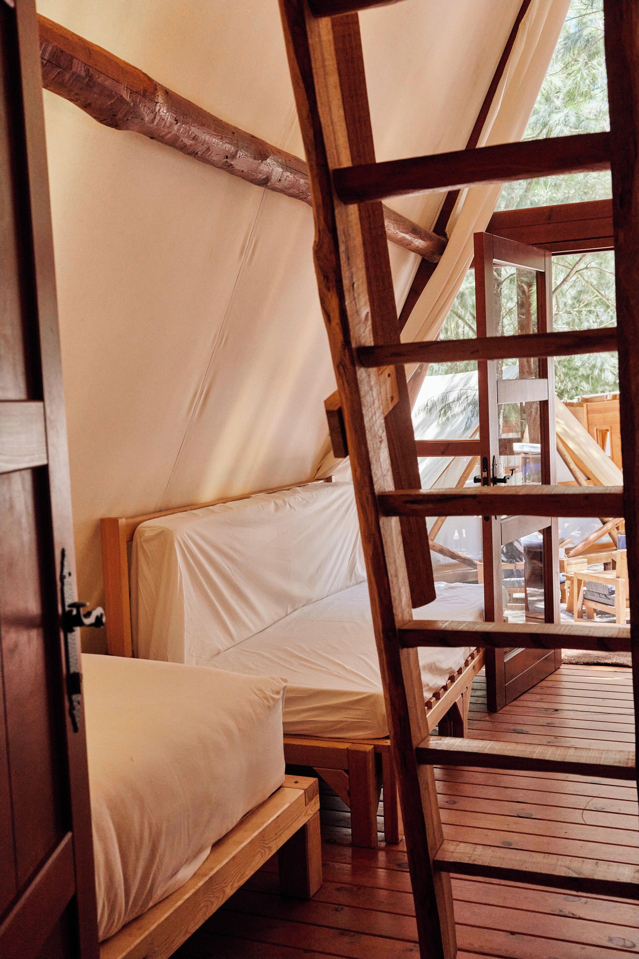 Un lit en bois avec un matelas blanc, installé dans une structure ressemblant à une tente.