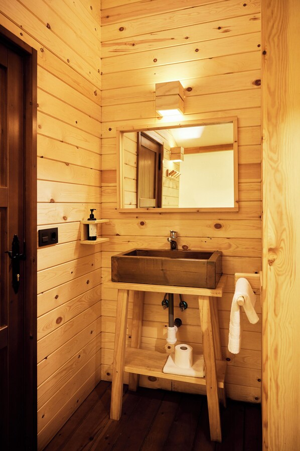 Baño de cabaña de madera con lavamanos de madera, un espejo y una toalla colgada en la pared.