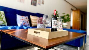 A wooden coffee table with a bottle of wine, two glasses, and decorative items in a living room with a blue sofa and a wall decorated with various pictures. - HUGE. FULL APARTMENT 100% REMODELED EXPO AREA (Zapopan)