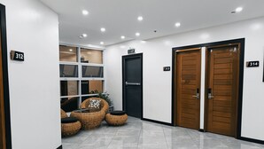 Een schone, moderne lobby met een receptiebalie, twee houten deuren en een zithoek met rieten meubilair.