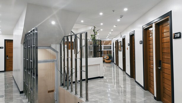 Een moderne hotellobby met een centrale trap, houten deuren met de nummers 318 en 319, en een duwdraaildeur onderaan de trap.