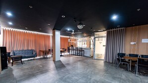 Een moderne hotellobby met een grijs betegelde vloer, een grijze bank, een houten salontafel en een bar met stoelen en een toonbank.
