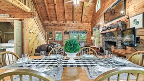 L’intérieur d’un chalet en bois comprend une table à manger dressée pour six personnes, une cheminée et un téléviseur fixé au mur.