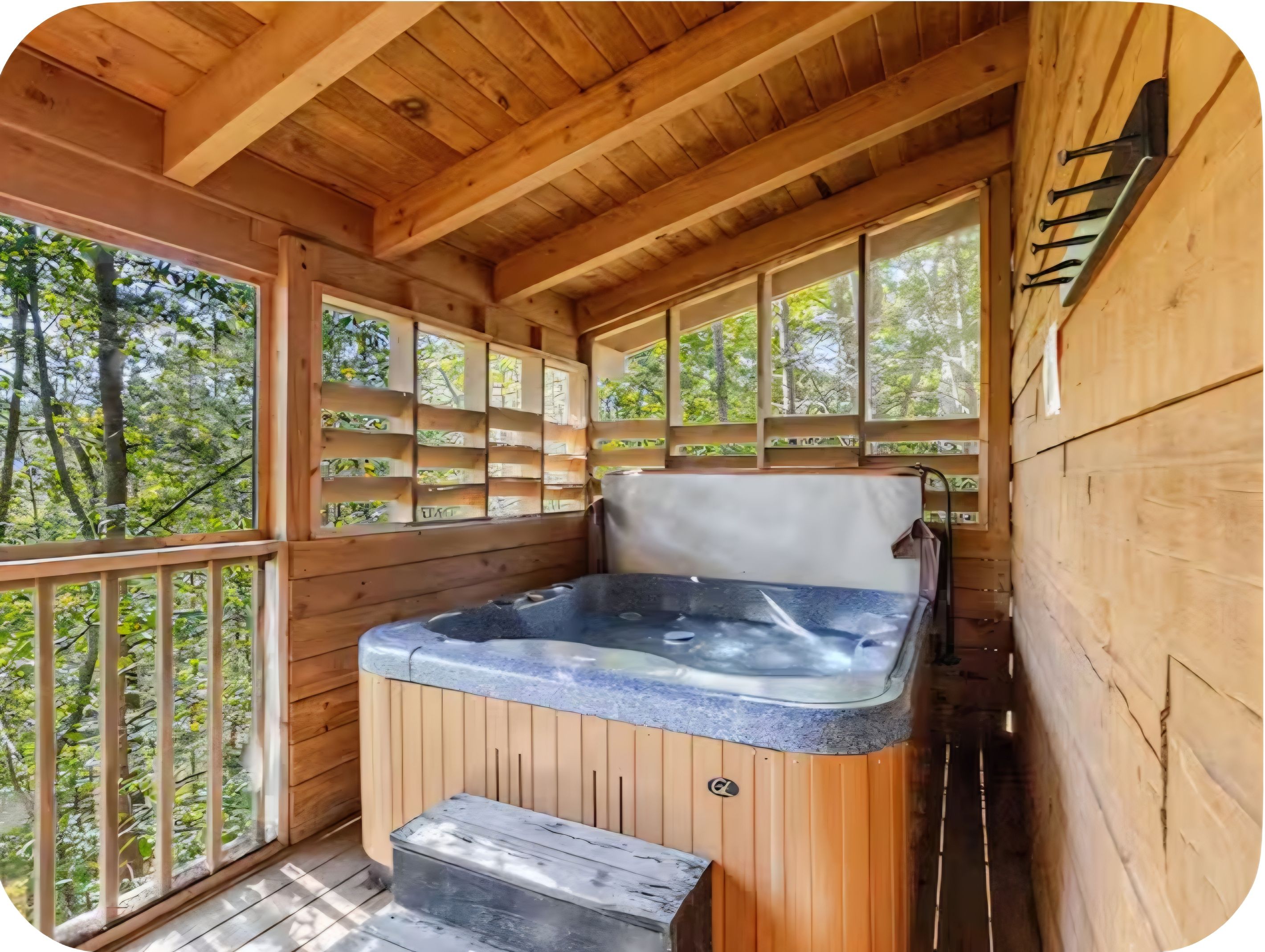 Une cabane en bois dotée d’un bain à remous, de murs en bois et d’un balcon offrant une vue sur les arbres.