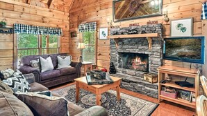 L’intérieur chaleureux d’un chalet avec une cheminée en pierre, des murs en bois et un coin salon confortable.