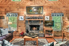 A cozy cabin interior with a stone fireplace, wooden walls, a comfortable seating area, and a television.