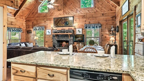Un intérieur de chalet chaleureux avec une cheminée en pierre, des murs en bois, un coin repas et une cuisine dotée de plans de travail en granit.