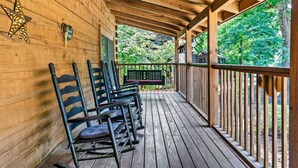 Une terrasse en bois, agrémentée d’une rangée de chaises et d’un banc, le tout entouré d’une balustrade en bois.