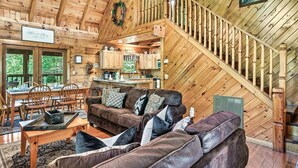 L’intérieur chaleureux d’un chalet avec un escalier en bois, un coin repas et un salon meublé d’un canapé en cuir marron et de coussins à motifs.
