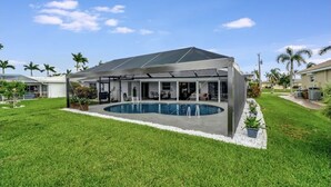 Ein modernes Haus mit überdachter Terrasse, Schwimmbad und gepflegtem Rasen.