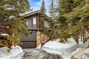 Une cabane dotée d’un escalier en pierre, entourée de neige et d’arbres à feuilles persistantes.
