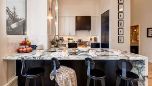 A modern kitchen with a marble island, black bar stools, and a large window.