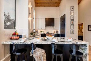 A modern kitchen with a marble island, black bar stools, and a large window.