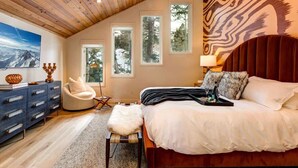 A bedroom with a wooden ceiling, a bed with white bedding, a chair, a dresser, and a painting on the wall.