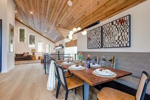 Un coin repas avec une table en bois, des chaises et un banc. Des œuvres d’art encadrées ornent le mur, et un escalier mène à un autre niveau.