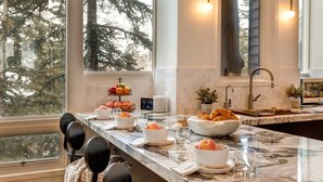 A kitchen with a marble countertop, a fruit bowl, a bowl of croissants, and a coffee maker.