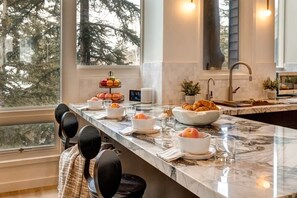 A kitchen with a marble countertop, a fruit bowl, a bowl of croissants, and a coffee maker.