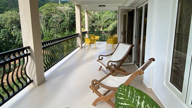 A balcony with two wooden lounge chairs and a table, overlooking a lush green landscape. - south hill villa (Mahe)